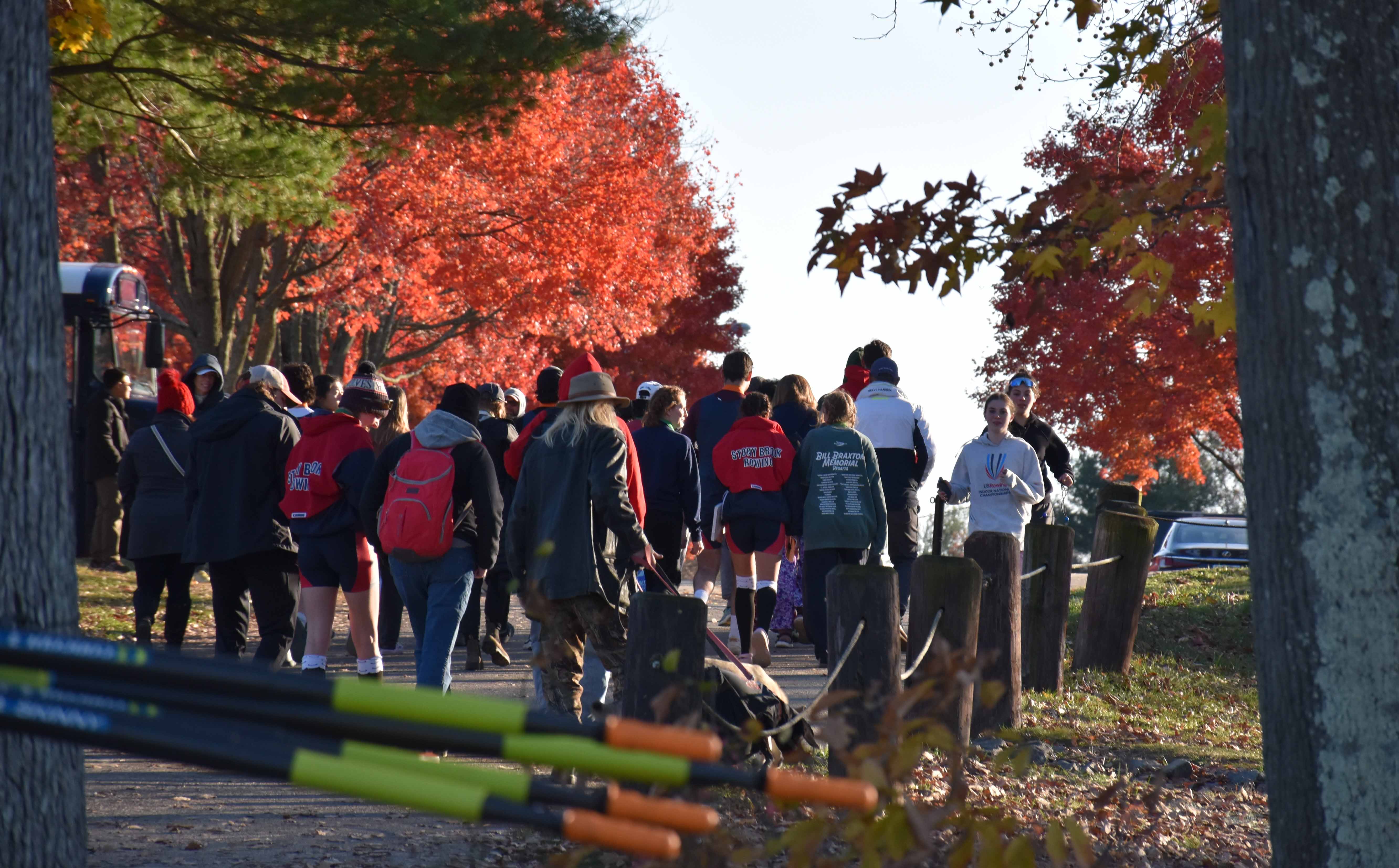 Stony Brook Crew members walking away, surrounded by fall-colored leaves and other regatta goers.